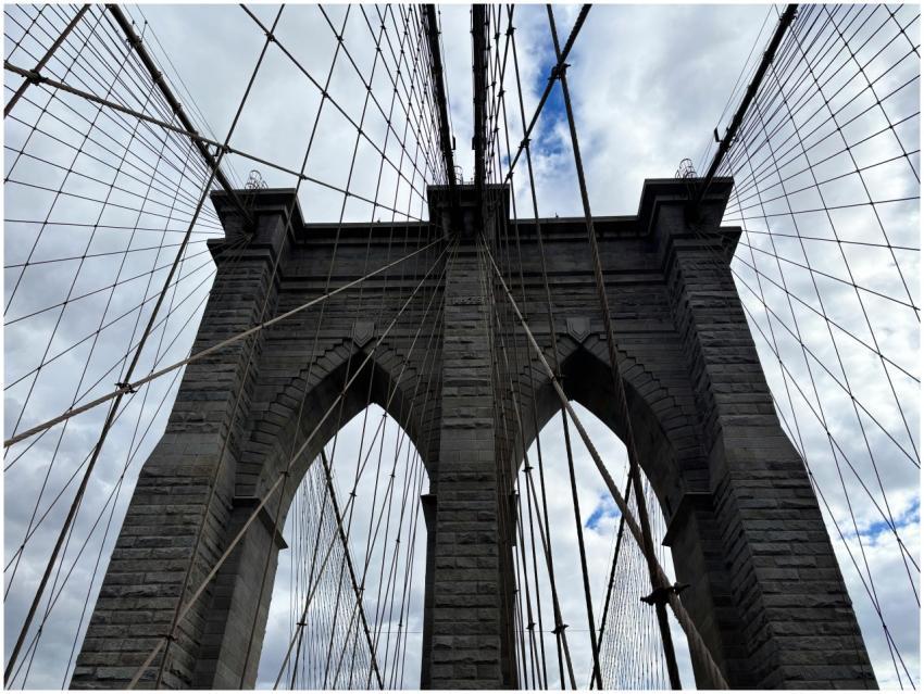 Iconic view of Brooklyn Bridge arches against clou