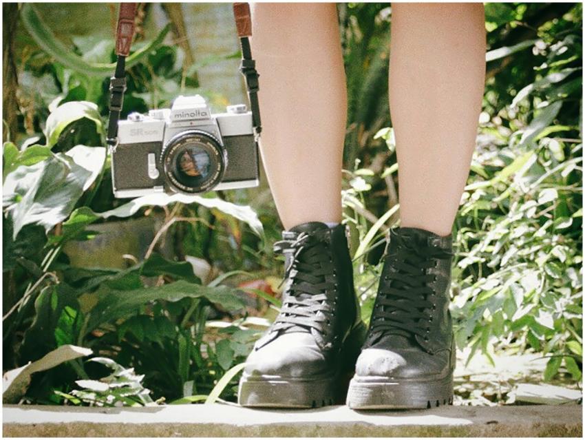 Legs with black boots and vintage camera in a lush