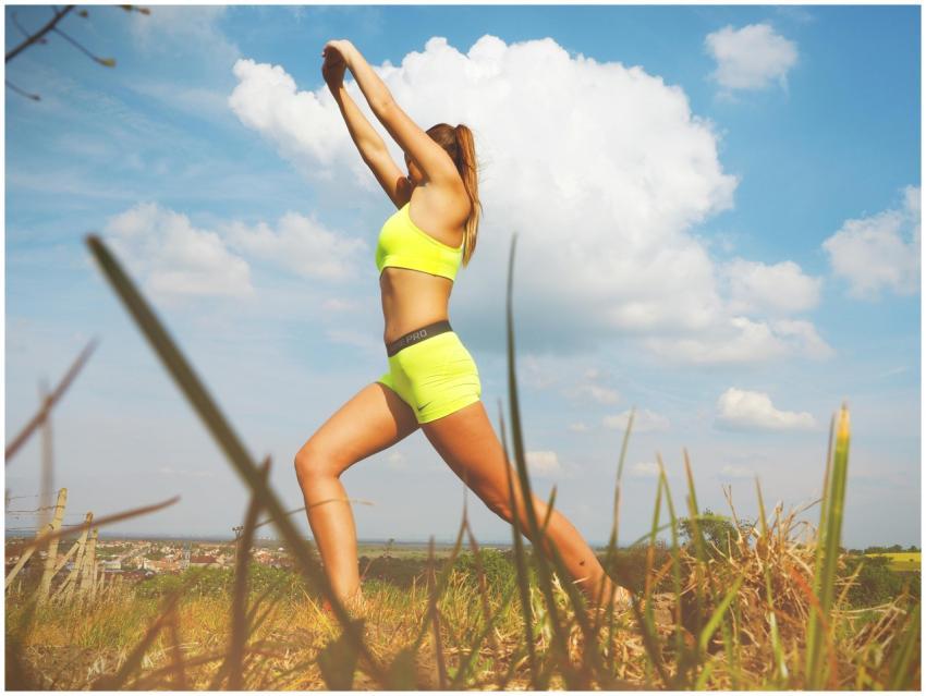 Athletic woman stretching in a field under blue sk