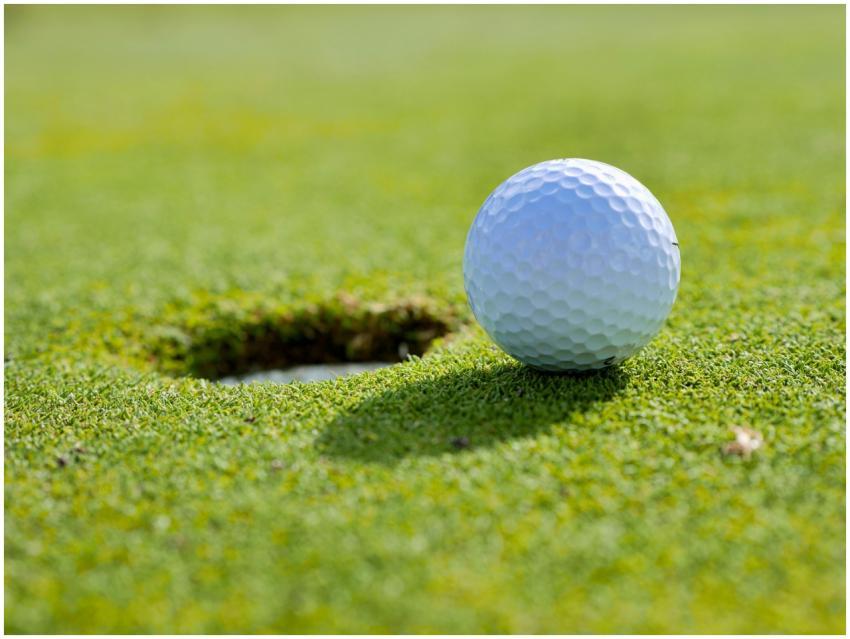 Close-up of a golf ball near the hole on a sunlit