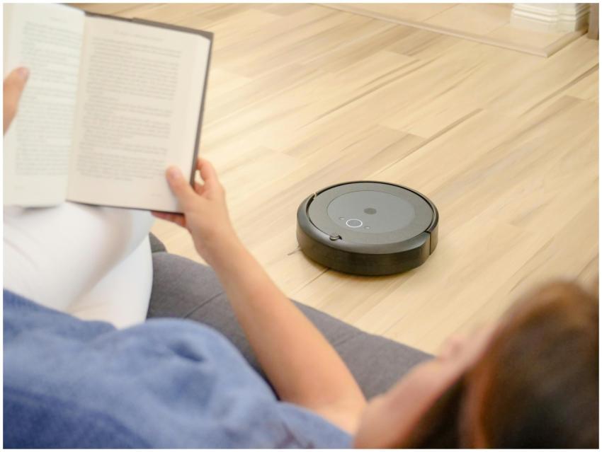 A woman relaxes on a sofa reading while a robotic