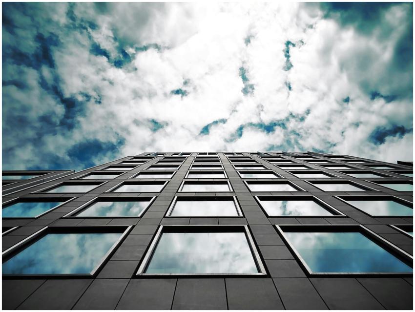 Low angle of a modern skyscraper reflecting clouds