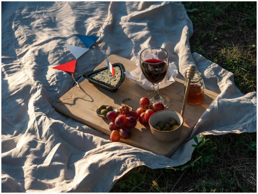 A sunlit picnic setup with French wine, cheese, gr