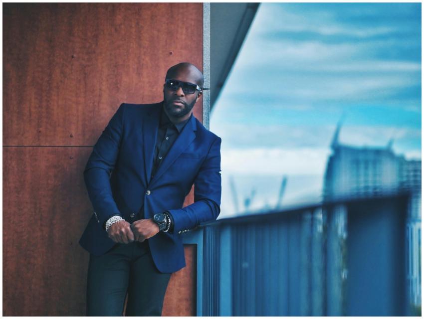 A fashionable man in a blue suit poses on a city b