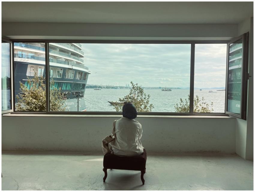 Woman sitting indoors gazing at sea through large