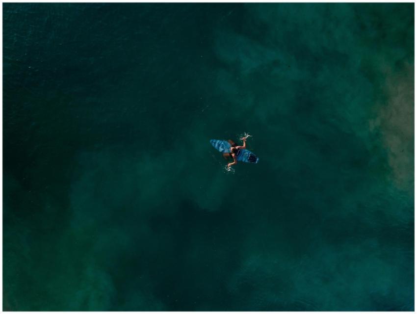 Aerial view of an unrecognizable surfer paddling o