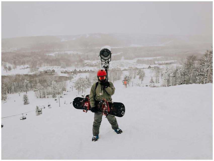 A snowboarder stands on a snowy slope with scenic