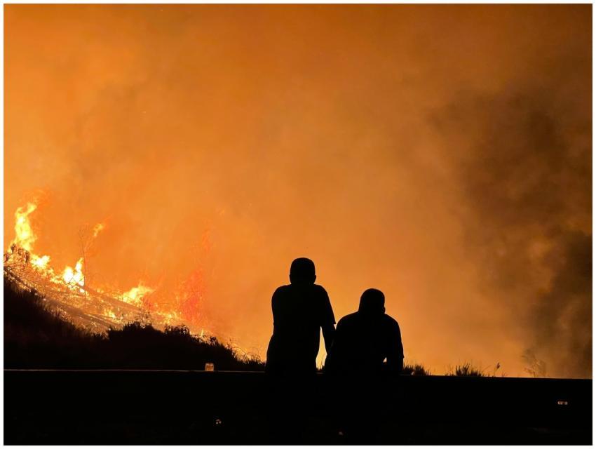 Two silhouettes observe a massive forest fire with