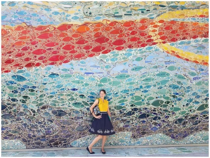 A woman posing against a colorful fish-themed mosa