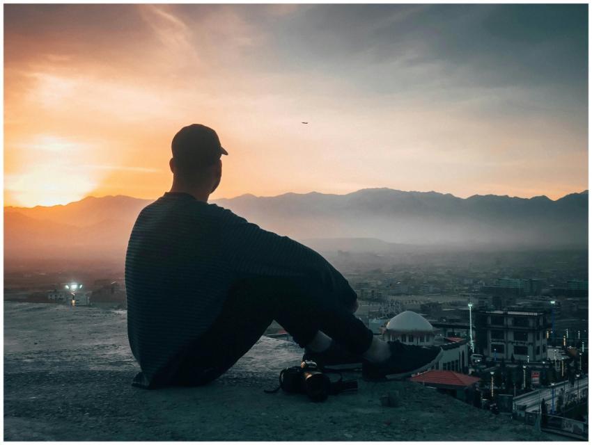 A person sits on a rooftop, silhouetted against a