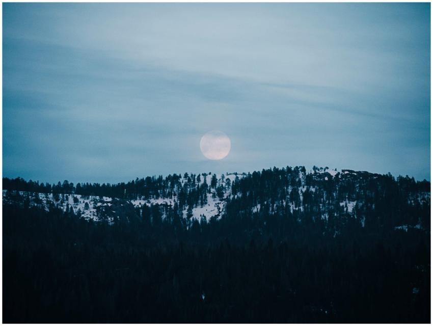 A serene view of a full moon rising over snowy mou