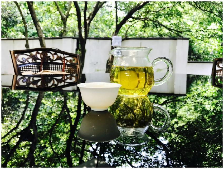 Green tea in a glass pitcher and cup on a reflecti