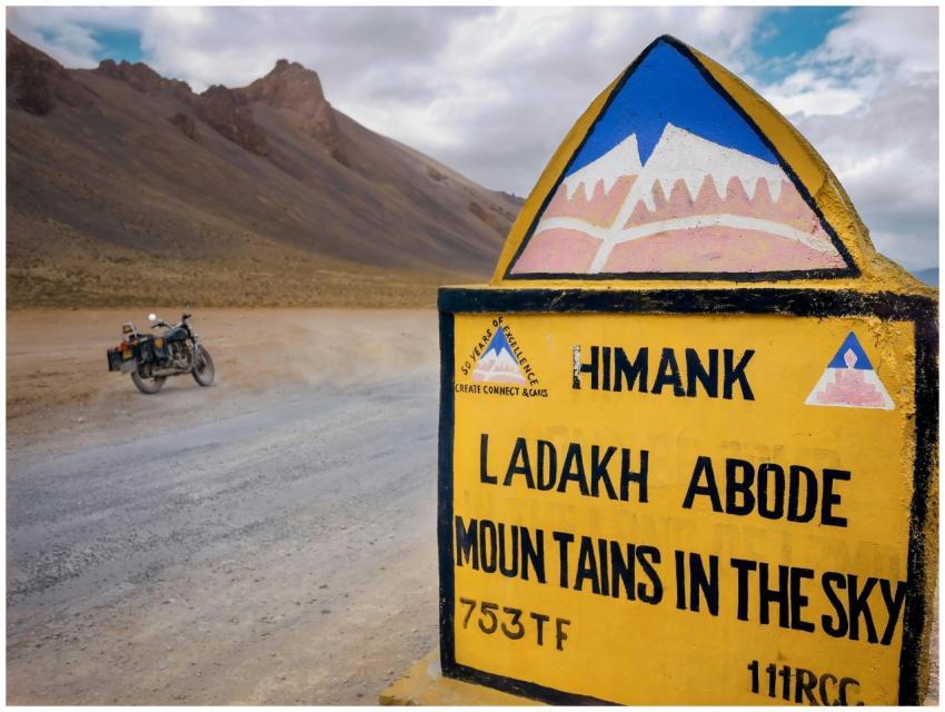 Road sign in Ladakh with motorcycle. Vast scenic m