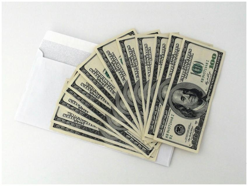 Fan of US $100 bills partially out of a white enve