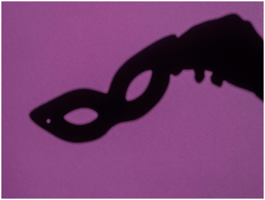 Silhouette of a hand holding a masquerade mask aga