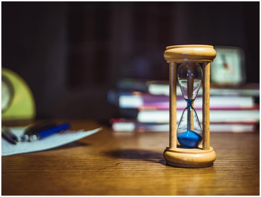 Close-up of a wooden hourglass on a desk, alongsid