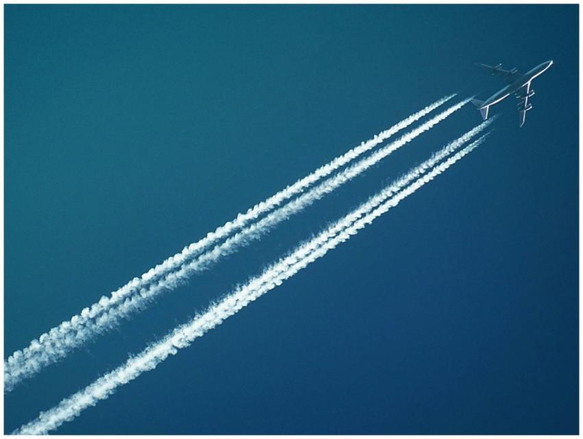 Aerial view of an airplane in flight, leaving vapo