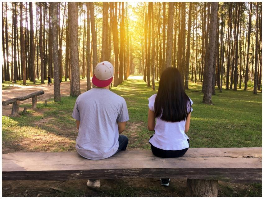 A young couple sits on a bench surrounded by tall
