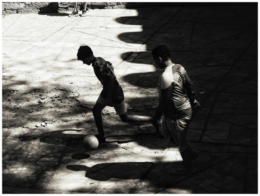 Two young boys playing soccer in a shadow-filled u