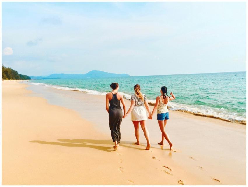 Three women walking hand in hand on a sandy beach