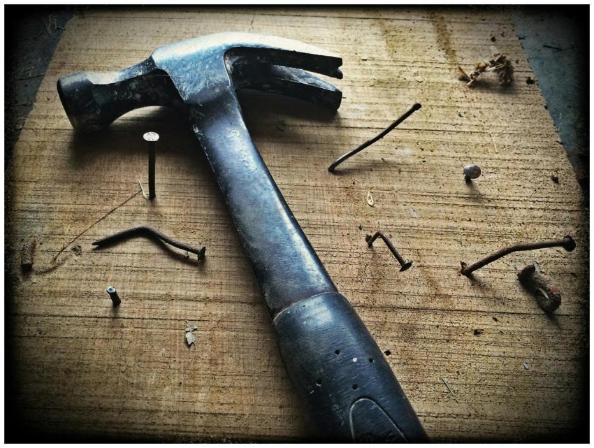 A weathered hammer surrounded by bent nails on a w