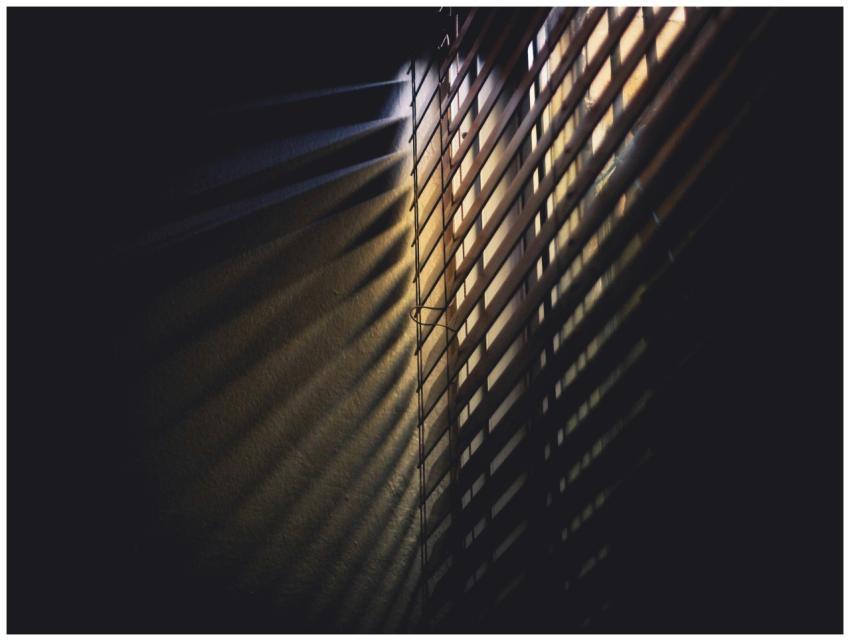 Dramatic light and shadows cast through window bli