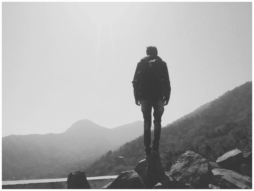 A lone hiker stands on rocks, overlooking misty mo