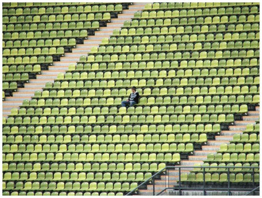 A solitary figure sits among green and yellow stad