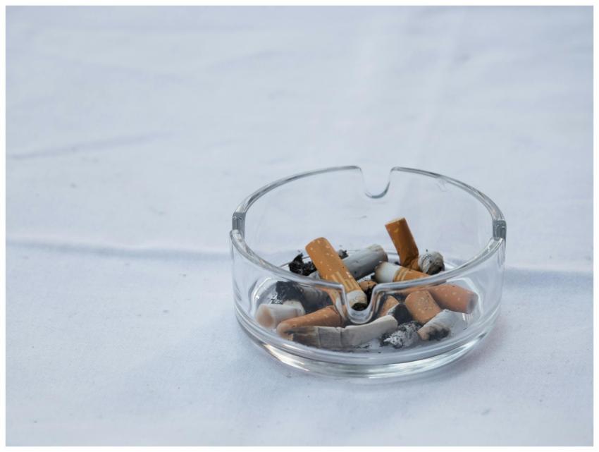 A clear glass ashtray filled with cigarette butts
