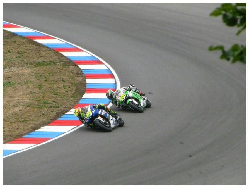 Two motorcyclists speed around a sharp corner on a