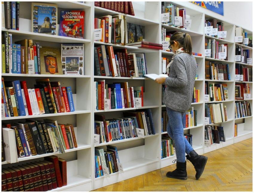 A young woman stands reading a book in a well-stoc