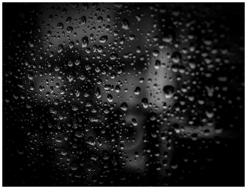 Close-up of raindrops on a glass surface with a da