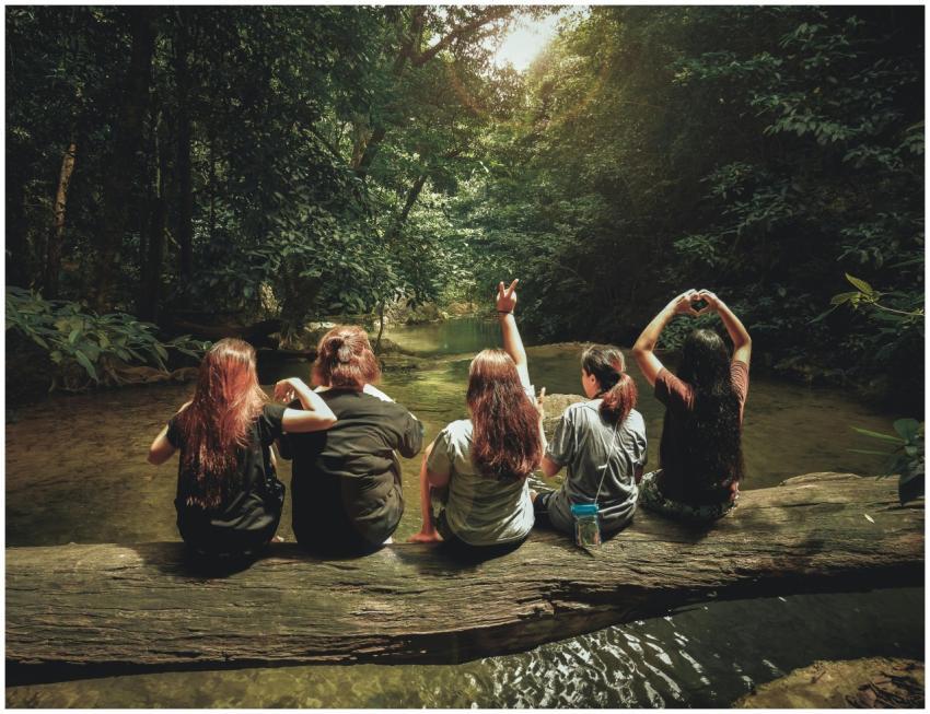 Five women enjoying nature on a log by a river in