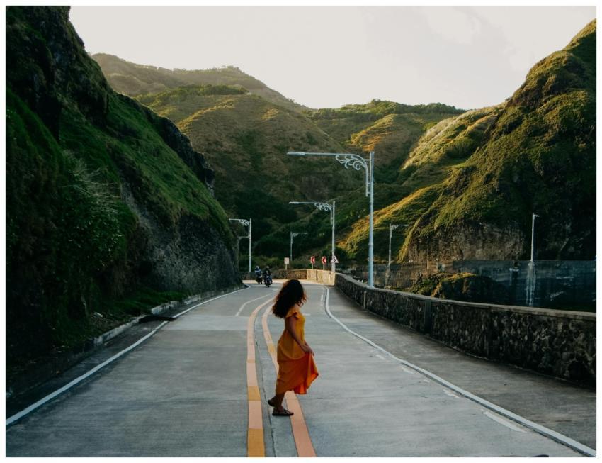 A woman in an orange dress walks along a scenic ro