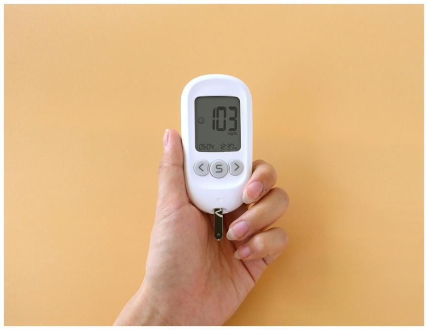 A hand holding a blood glucose meter displaying 10