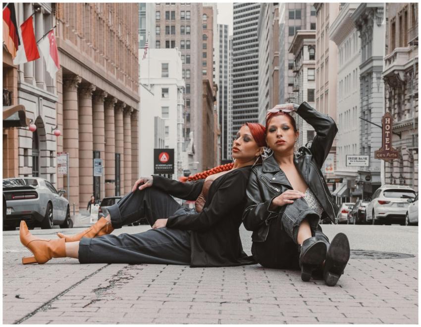 Two stylish women pose back-to-back on a city stre