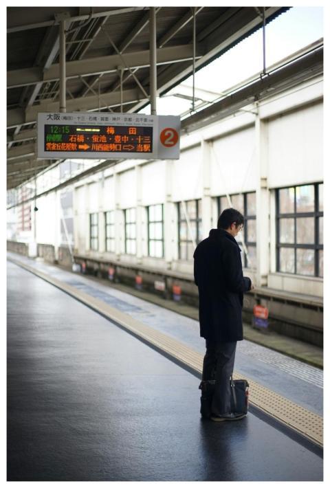 Person waiting at a train station platform, checki