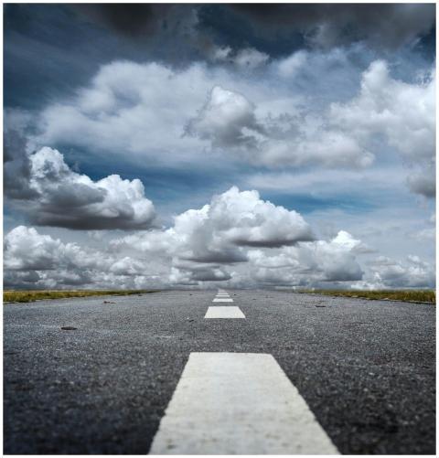 A straight road stretched toward a dramatic sky fi