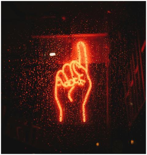 A vibrant neon hand sign seen through a wet window