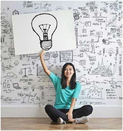 Young woman holds a light bulb drawing against a c