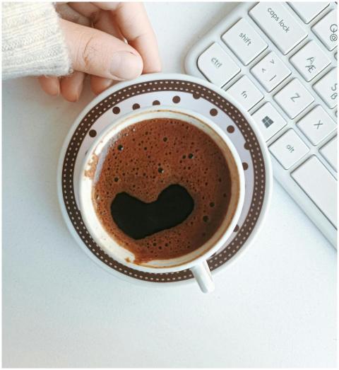 A hand holding a cup of coffee with a heart shape,