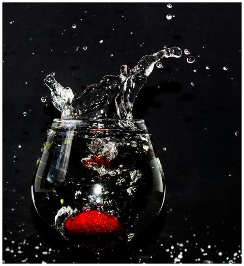 A strawberry splashes into a glass of water, creat