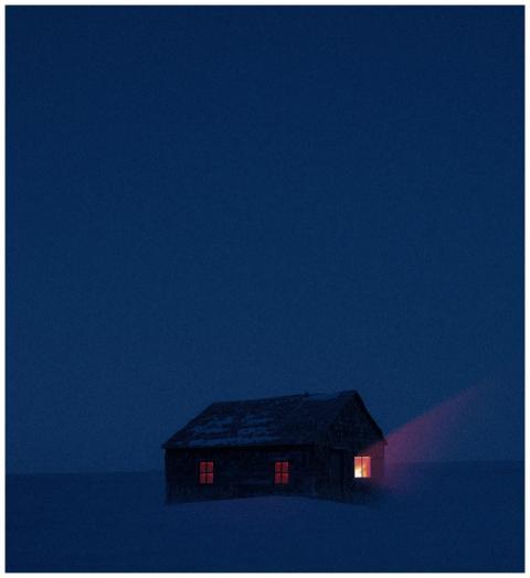 A solitary cabin with glowing windows in a snowy l