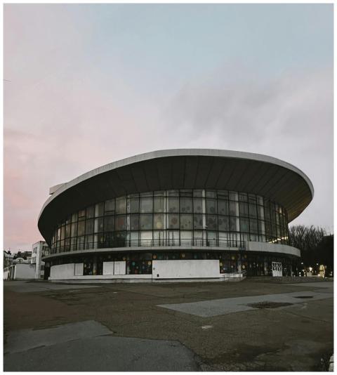 Circular building with glass facade under a pastel