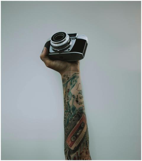 A tattooed arm raises a vintage camera against a p