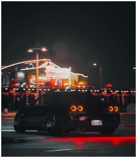 A black sports car parked under city lights at nig
