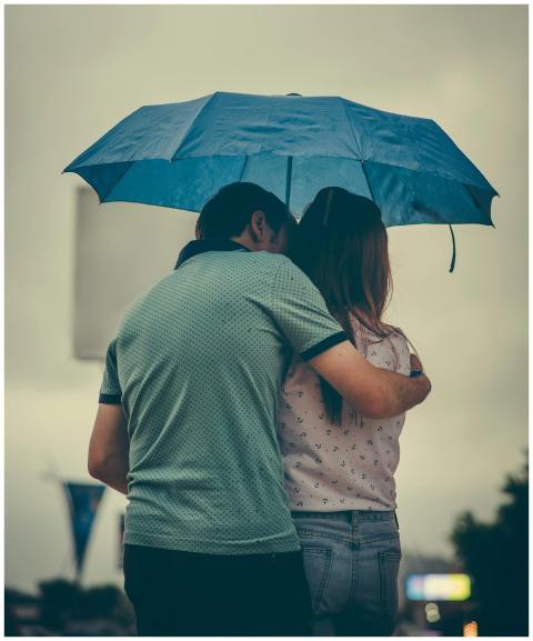 A couple embraces under a blue umbrella in a rainy
