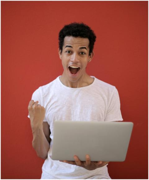 Young man in white shirt with laptop, celebrating