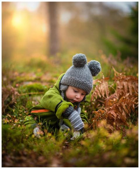 A cute baby in a knit hat and green outfit explori