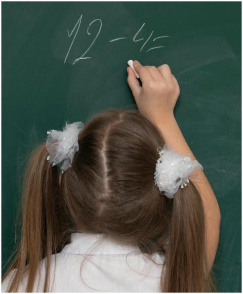 Young girl writing a subtraction problem on a chal